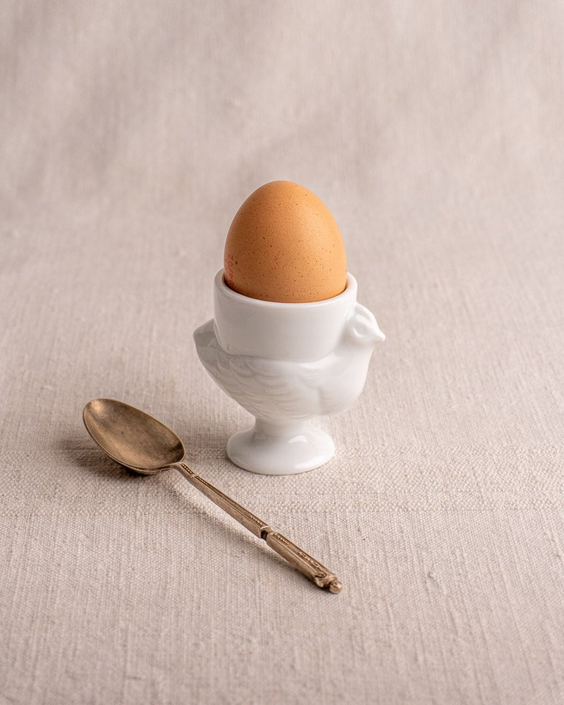 Vintage French opaline glass egg cup with brown egg and silver spoon on beige fabric.