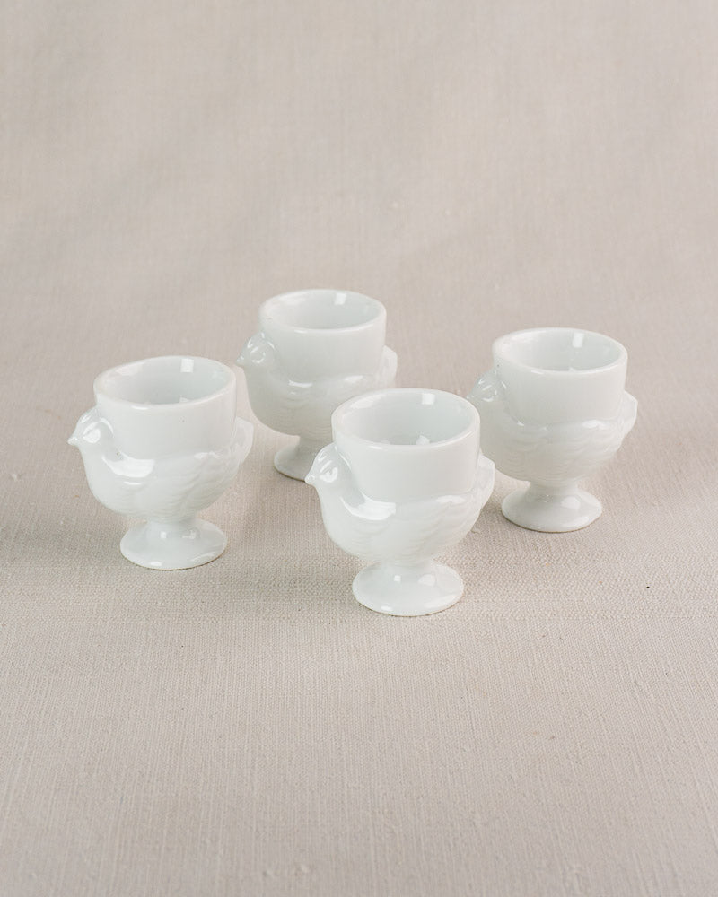 Set of four vintage French opaline glass hen egg cups with classic wing and tail details on neutral surface.