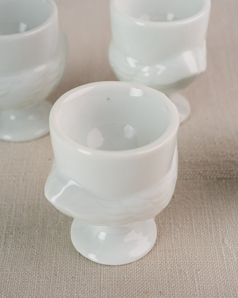 Set of four vintage French opaline glass egg cups with swirl design and pedestal base on beige surface.