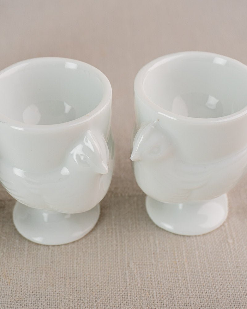 Set of four vintage French opaline glass hen-shaped egg cups with delicate wing and beak details.