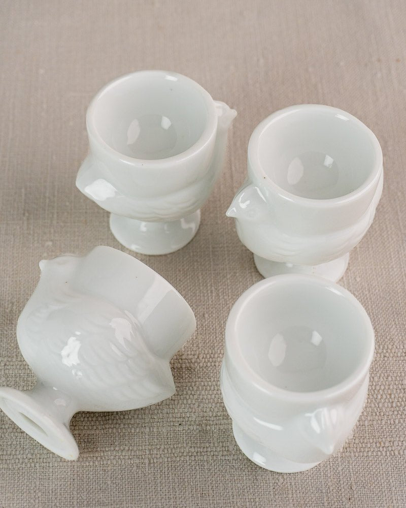 Set of four vintage French opaline glass hen-shaped egg cups with detailed wings, on beige surface.