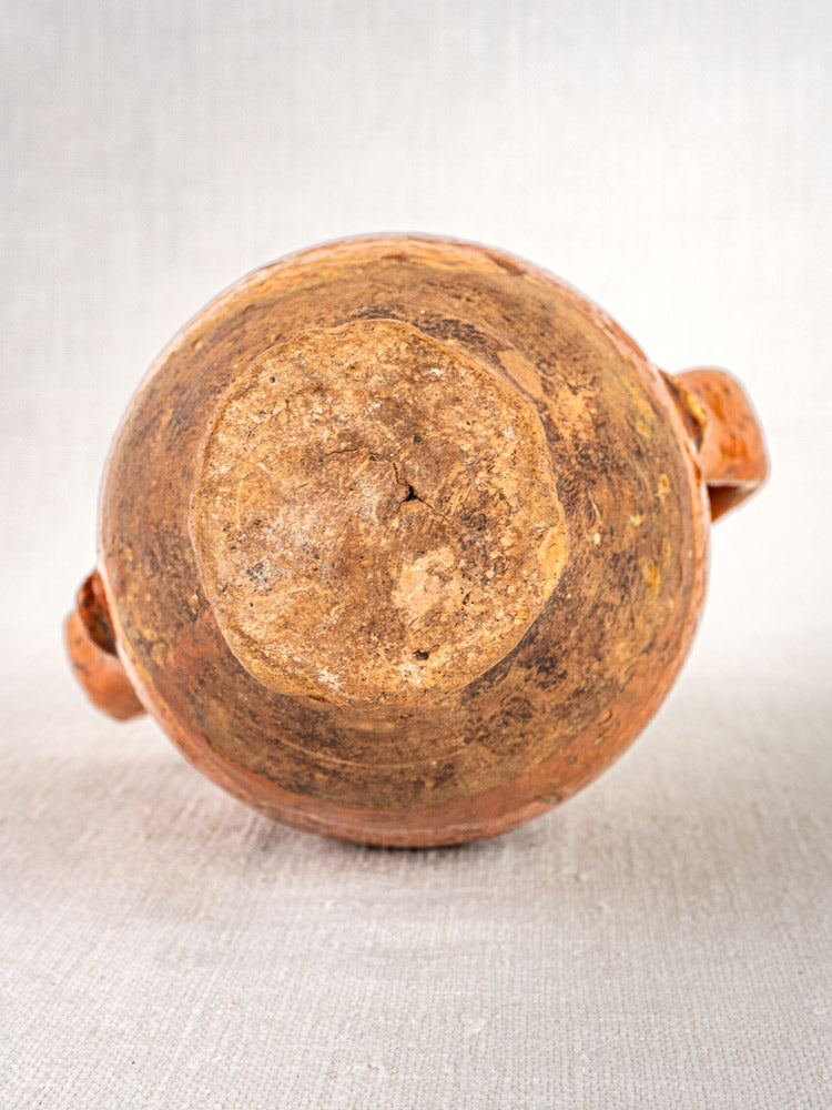 Antique French terracotta wine gourde shown from below with textured unglazed base, neutral fabric backdrop.