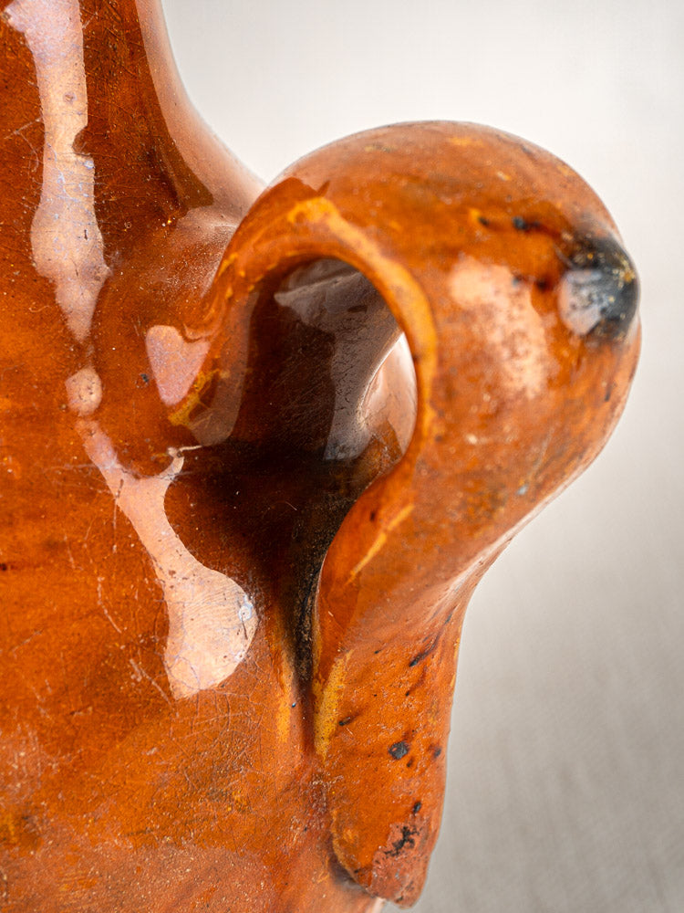Curved glossy orange terracotta handle with textured details on an antique French wine gourde.