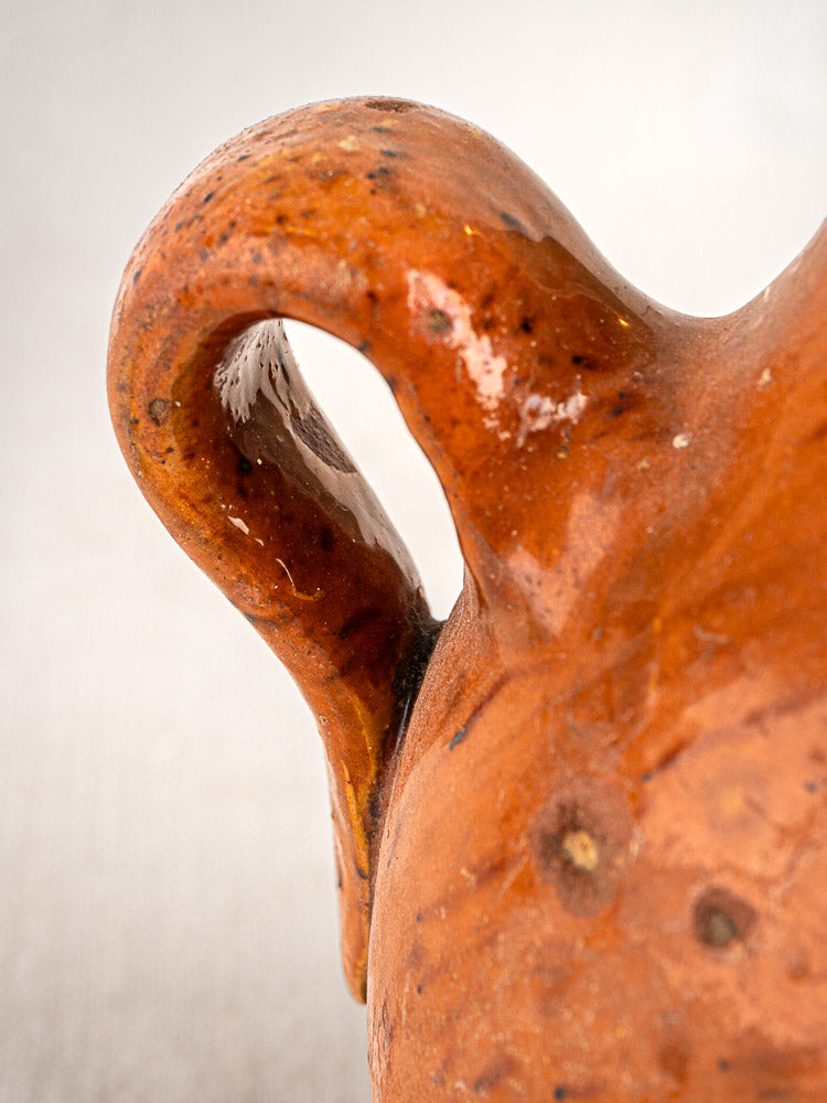 Curved handle of antique French wine gourde with glazed brown ceramic and textured details, softly blurred background.