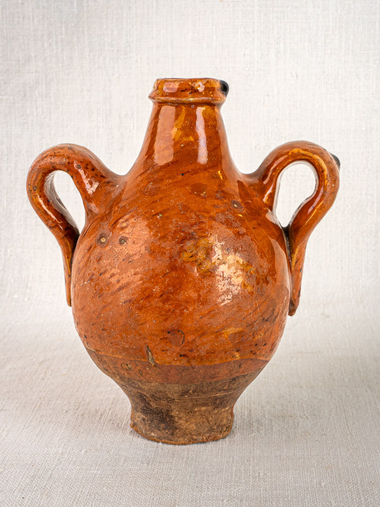 Antique French terracotta wine gourde with side handles, rustic orange-brown glaze, light textured backdrop.