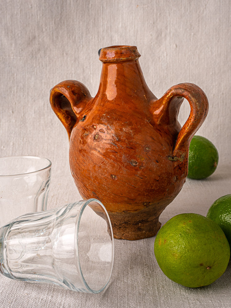 Antique French terracotta wine gourde with side handles, rustic orange-brown glaze, light textured backdrop.