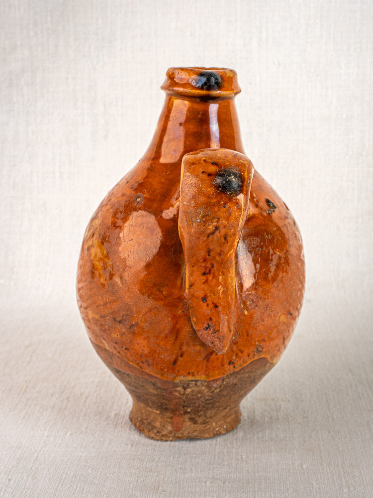 Antique French wine gourde with textured brown glazed terracotta, rounded body, and dual handles on neutral fabric.