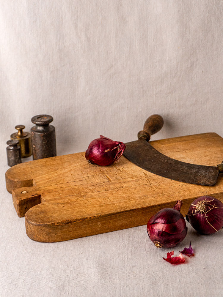 Antique French hardwood cutting board with double-lobed shape, worn surface, and hanging hole on gray background.