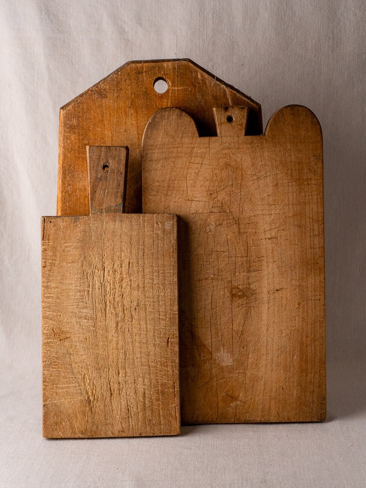 Antique French double-lobed hardwood cutting board with vintage patina set against a neutral fabric backdrop.