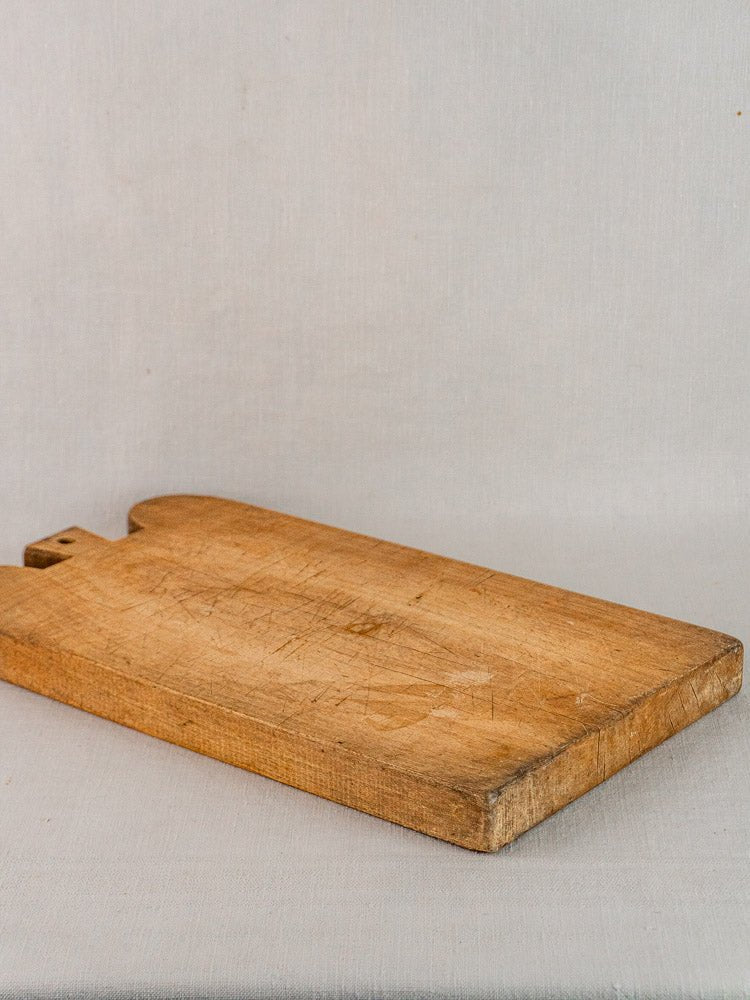 Antique French double-lobed hardwood cutting board with knife marks on light gray fabric surface.