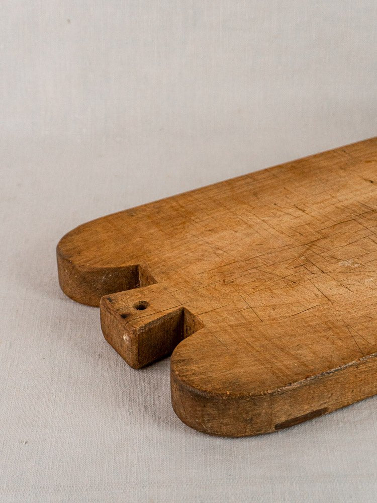 Antique French double-lobed hardwood cutting board with rounded corners and knife marks on light fabric.