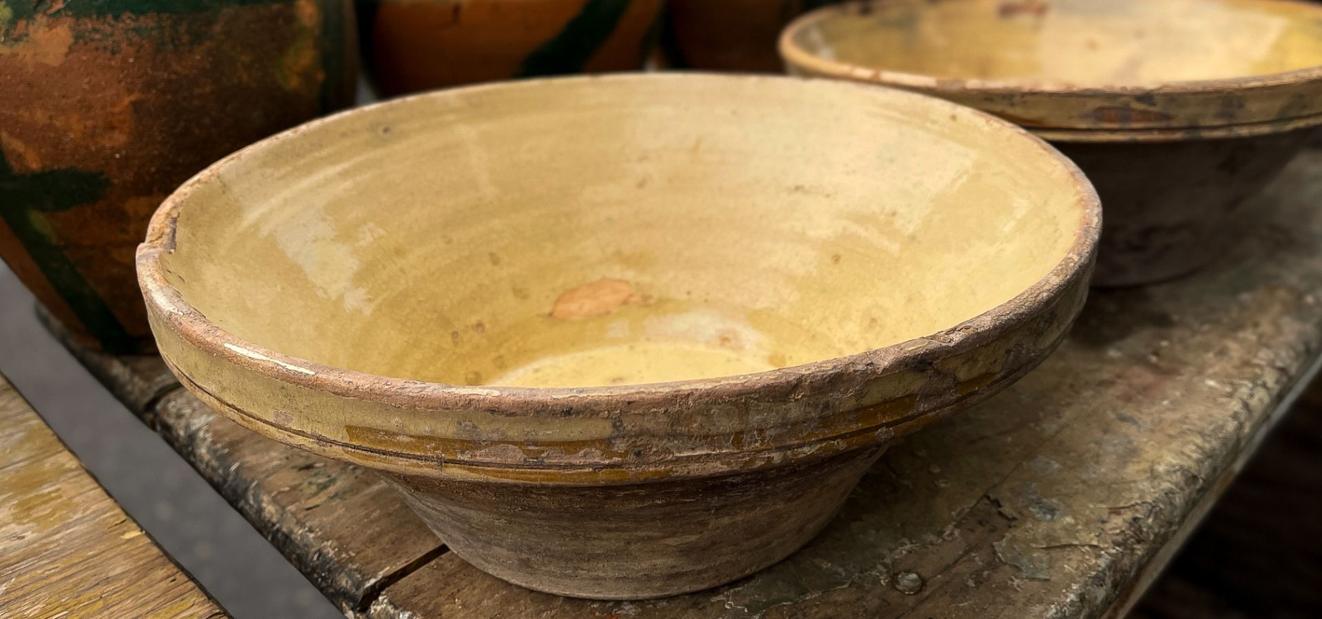 Vintage French yellow-glazed tian bowl displayed on a weathered wooden table at a market in Provence.