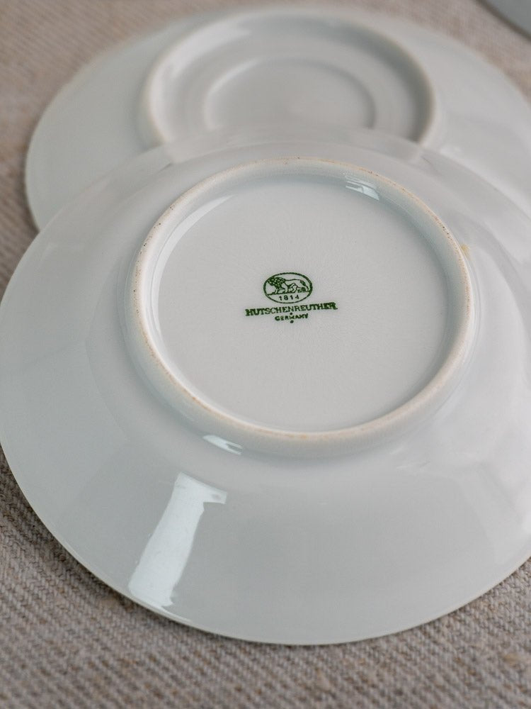 Pair of white Hutschenreuther porcelain saucers, one showing green Germany hallmark on textured surface.