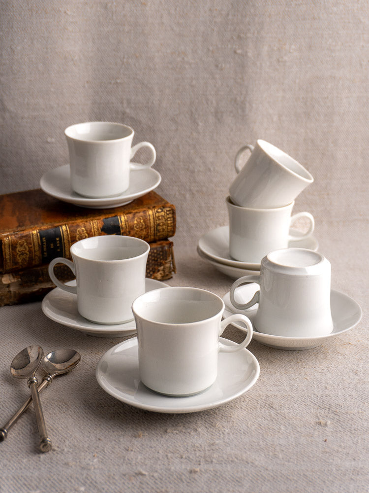Set of six white porcelain Hutschenreuther espresso cups and saucers arranged on beige textured surface.