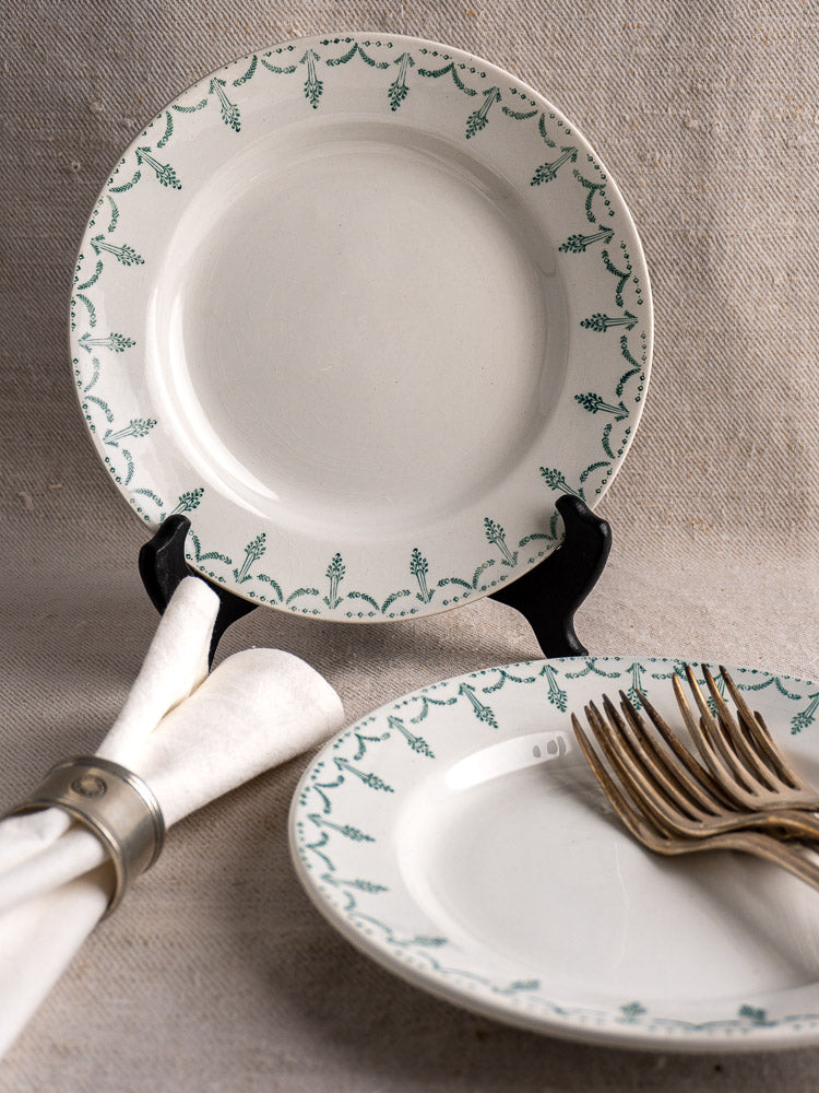 Antique French Gien porcelain plates with green garland border, displayed on beige linen with silver napkin ring.