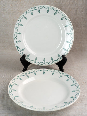 Antique French Gien porcelain plates with green garland border, displayed on stand and beige fabric.