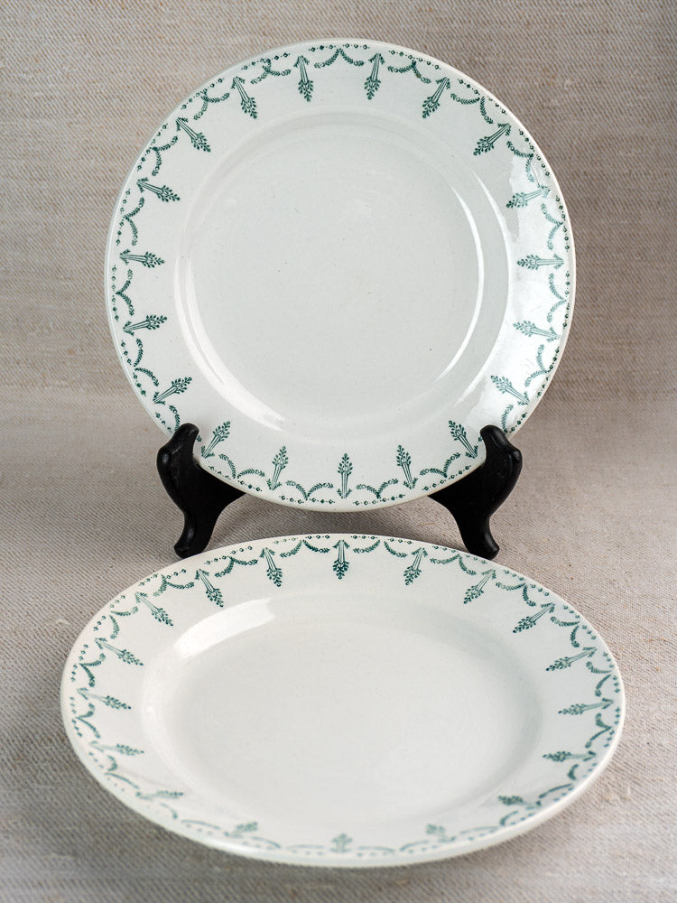 Antique French Gien porcelain plates with green garland border, displayed on stand and beige fabric.