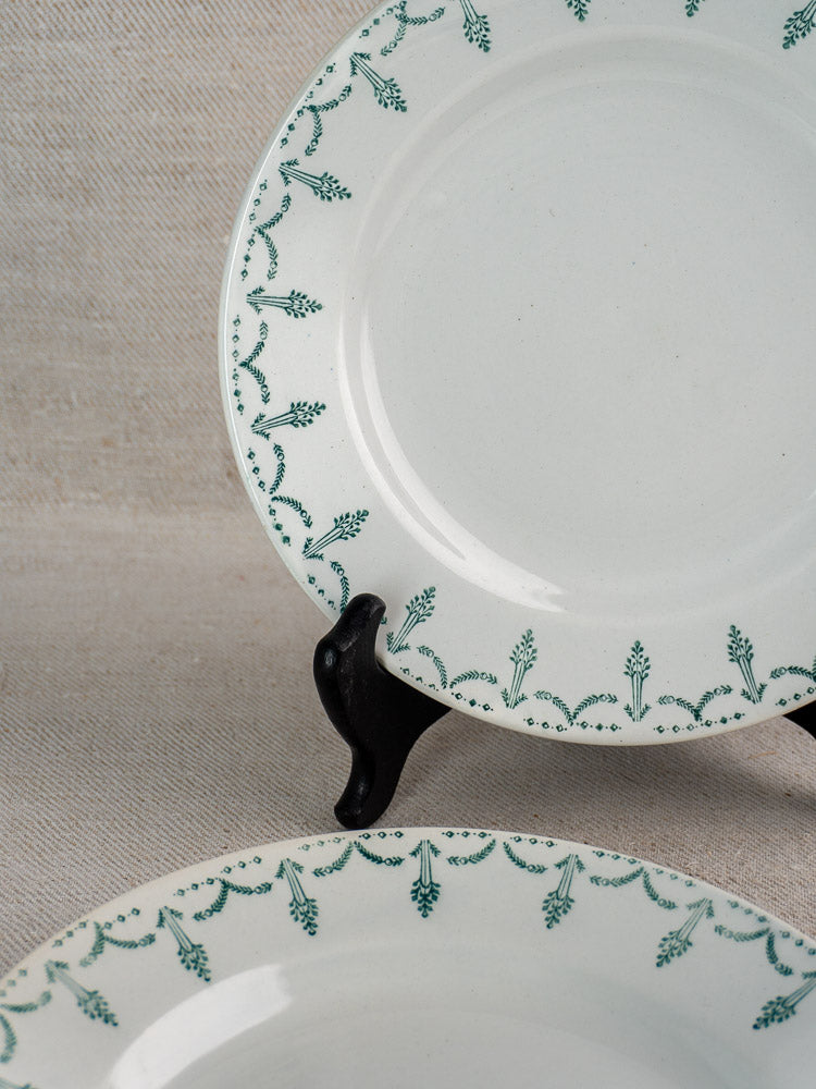Antique French Gien porcelain plates with green garland border, one upright on black stand.
