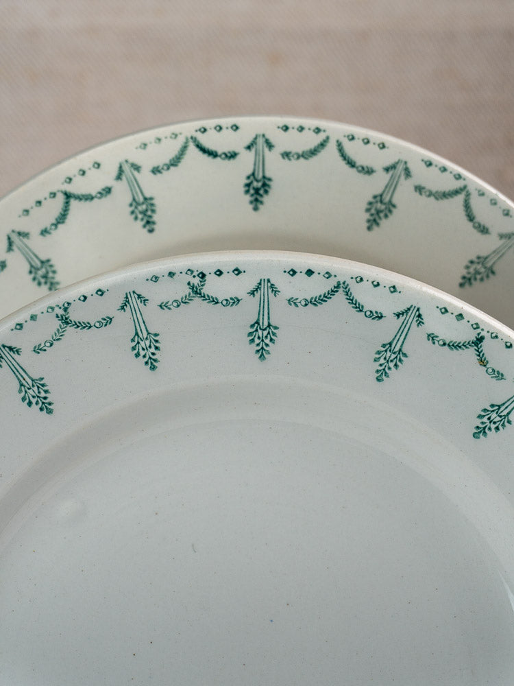 Pair of antique French Gien porcelain plates with green garland borders, partially overlapping on neutral background.