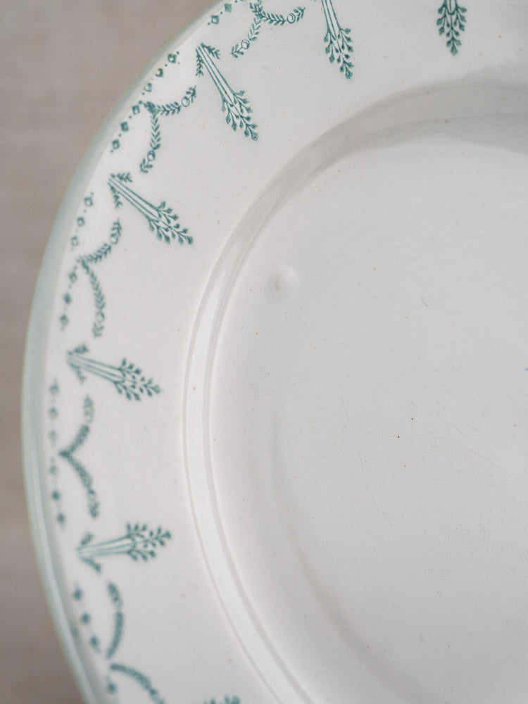 Antique French Gien porcelain plates with green garland borders, early 20th century, on beige background.