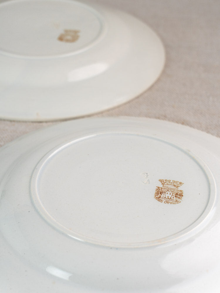 Antique French Gien porcelain plates with green garland border, shown upside down on light fabric.