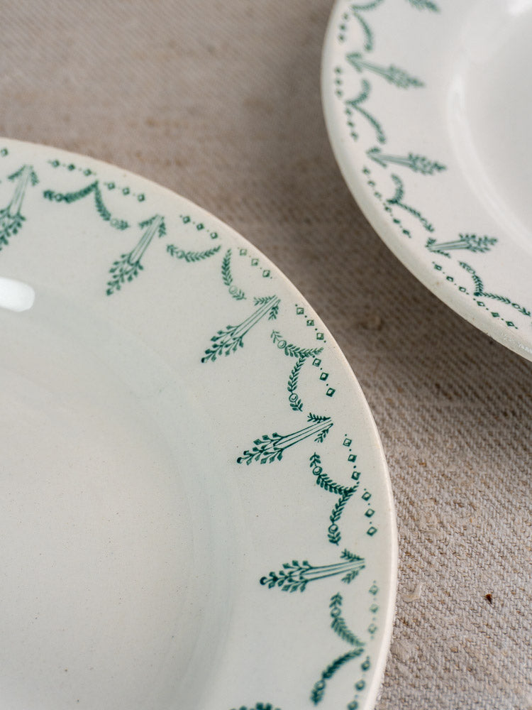 Antique French Gien porcelain plates with green garland borders on a beige textured surface.