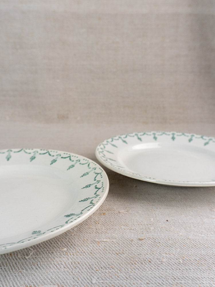 Pair of antique French Gien porcelain plates with green garland border on beige textured fabric.