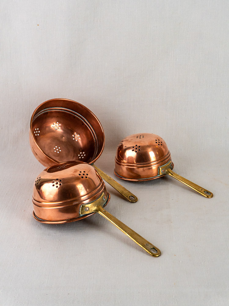 Antique French copper colander trio with brass handles displayed on a neutral background.