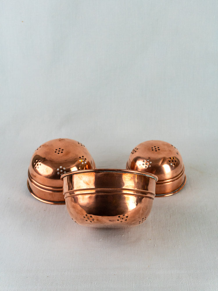 Three polished French copper passoires from an antique nesting colander trio on a light fabric background.
