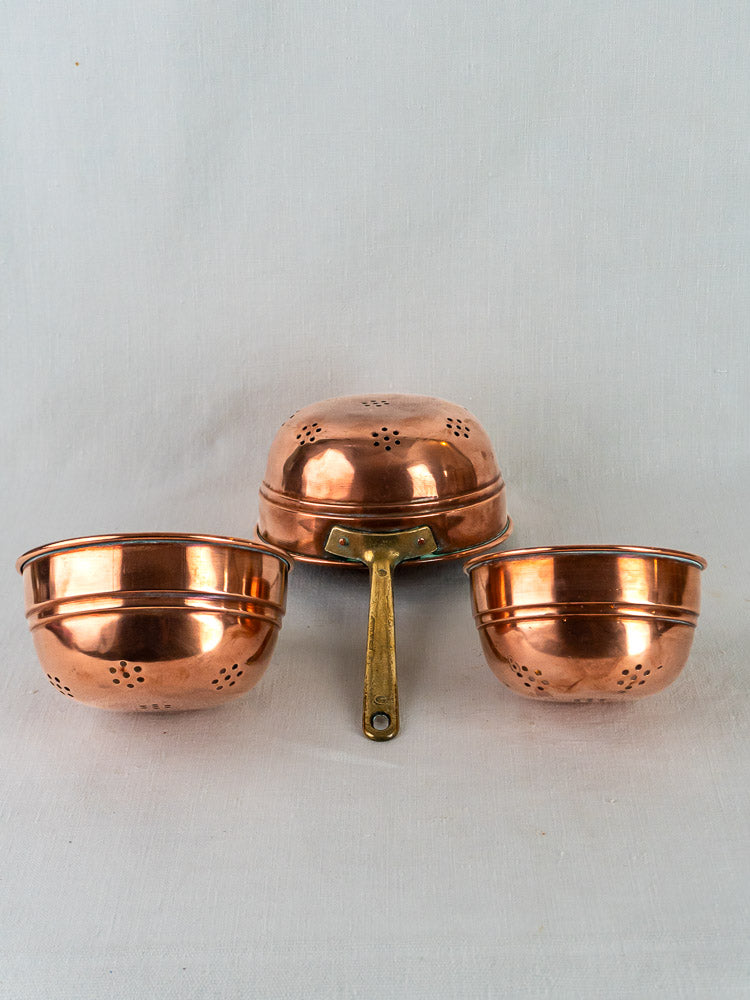 Trio of antique French copper passoires with brass handles displayed on a white background.