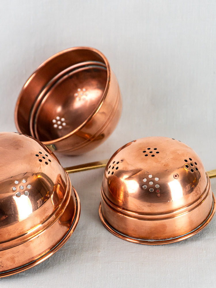 Antique French copper passoires with perforated domed lids, arranged on a plain light background.