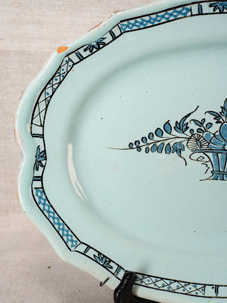 Antique French faience platter with pale blue Rouen floral motifs, blue border, minor edge chipping, displayed on a stand.