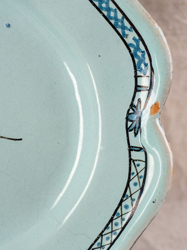 Antique French faience platter in light blue with scalloped edge, blue and black border, small rim chip; neutral background.