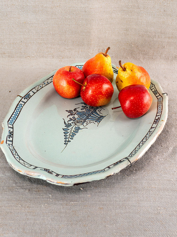 Antique French faience platter with blue floral pattern, displayed with apples and pears on beige textured fabric.