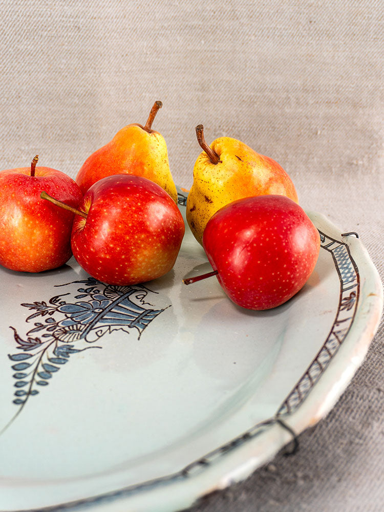 Antique French faience Cul Noir platter with three red apples and two yellow pears on neutral fabric.