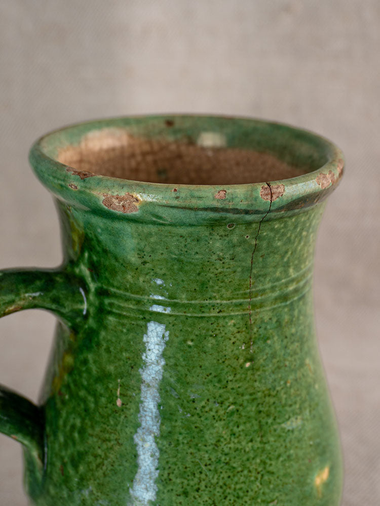 Antique French green-glazed earthenware petite cruche with worn edges, glaze imperfections, and a crack near the rim.