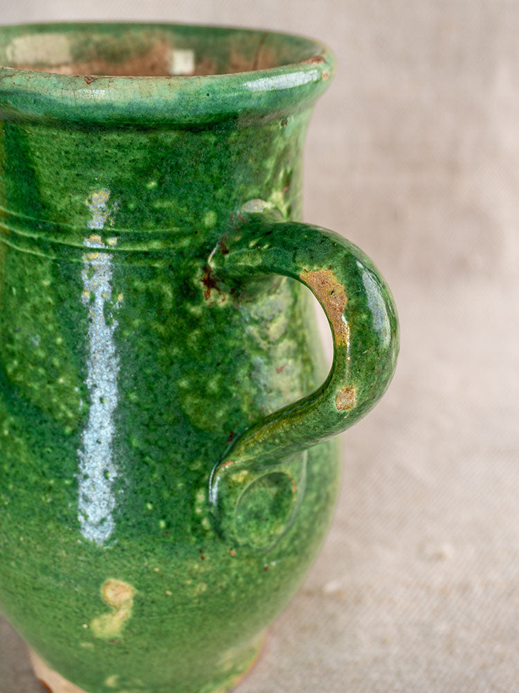 Antique French green glazed earthenware petite cruche with curved handle, rustic finish, on neutral fabric background.
