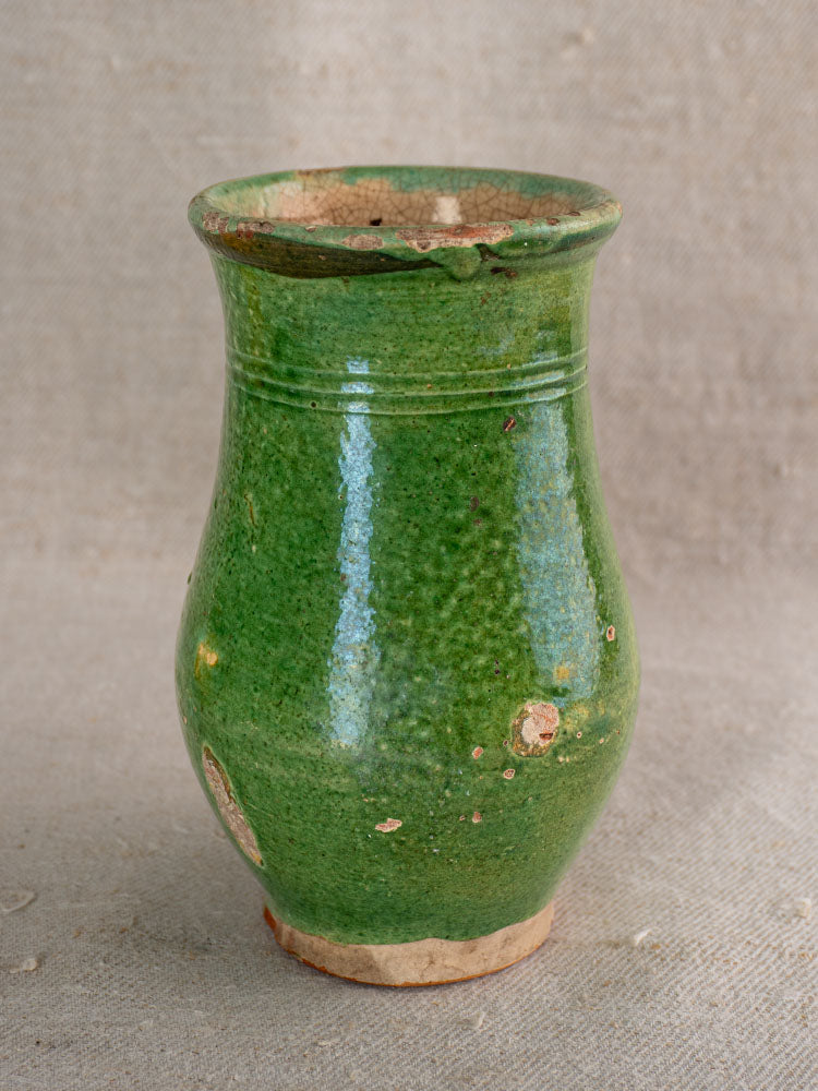 Antique French green glazed earthenware petite cruche with flared rim and gentle wear, on neutral textured fabric.