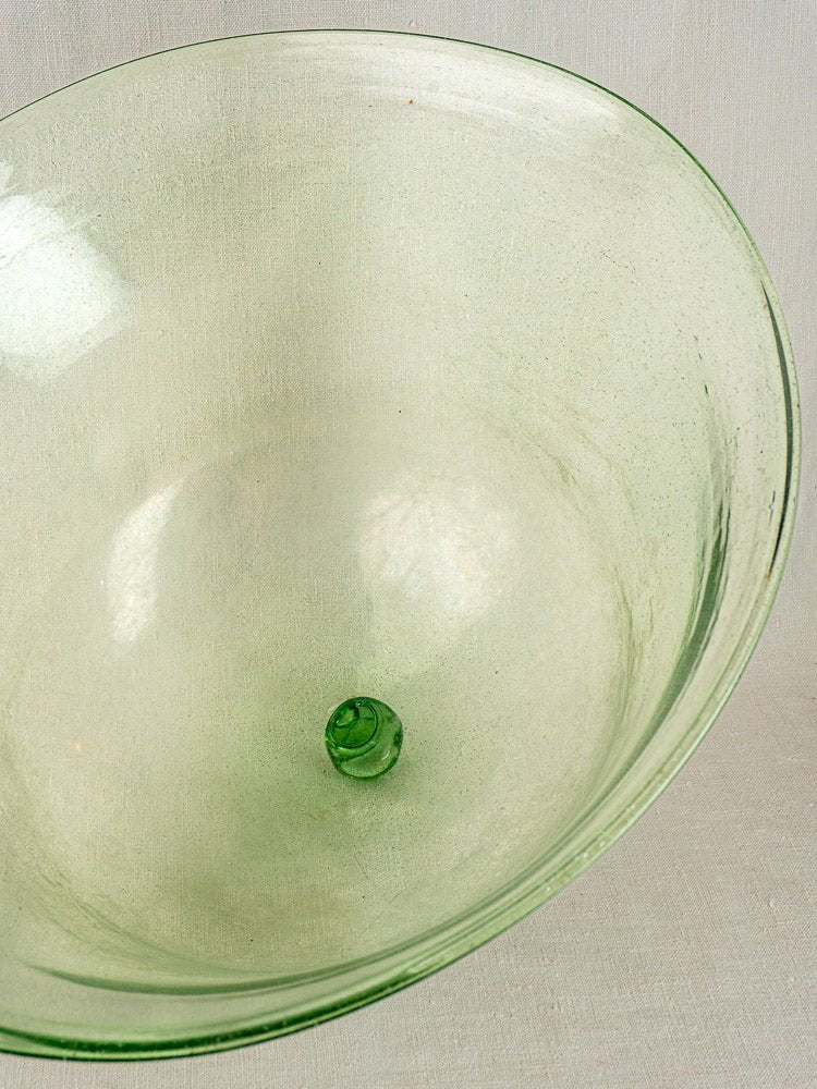 Hand-blown pale green antique French glass garden cloche with smooth surface and rounded base on neutral fabric.