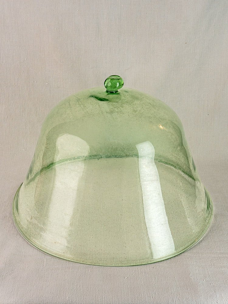 Antique French hand-blown pale green glass garden cloche with rounded handle on light beige fabric background.