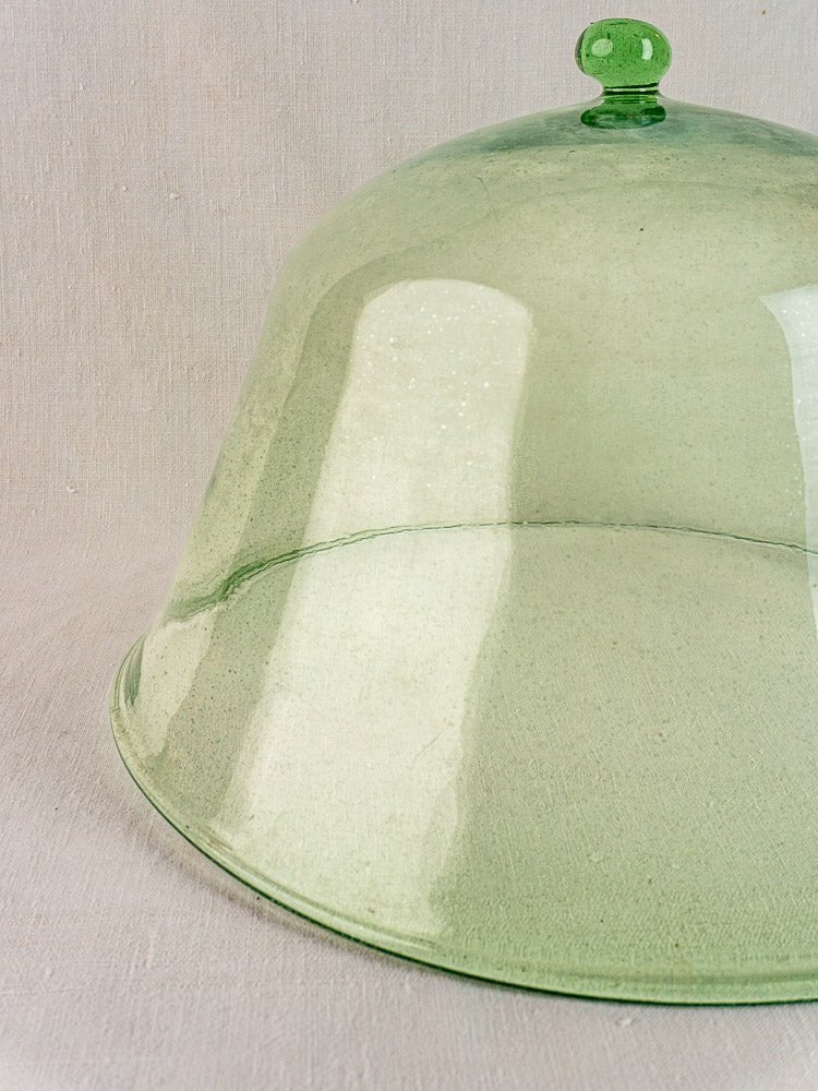 Antique 19th-century French hand-blown pale green glass garden cloche on a light beige textured surface.