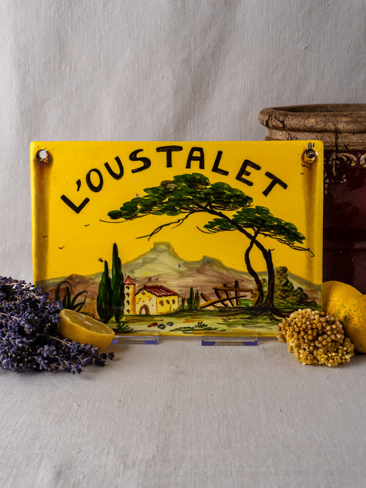 Yellow French faience plaque with hand-painted Provençal landscape, displayed amid dried flowers and lemon.