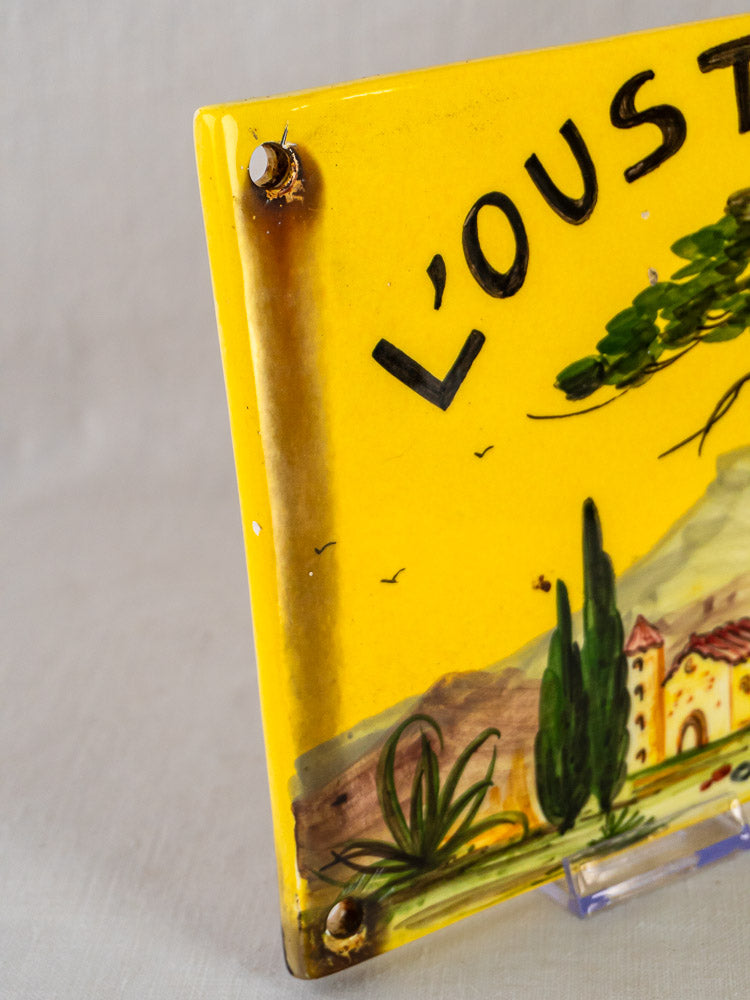 L’Oustalet French faience house plaque with hand-painted Provençal landscape, rusty screws, and edge discoloration.
