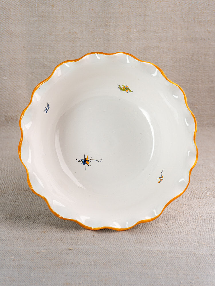 Pair of vintage French Moustiers-style faience compotes with yellow-edged scalloped rims and insect motifs, on neutral fabric.