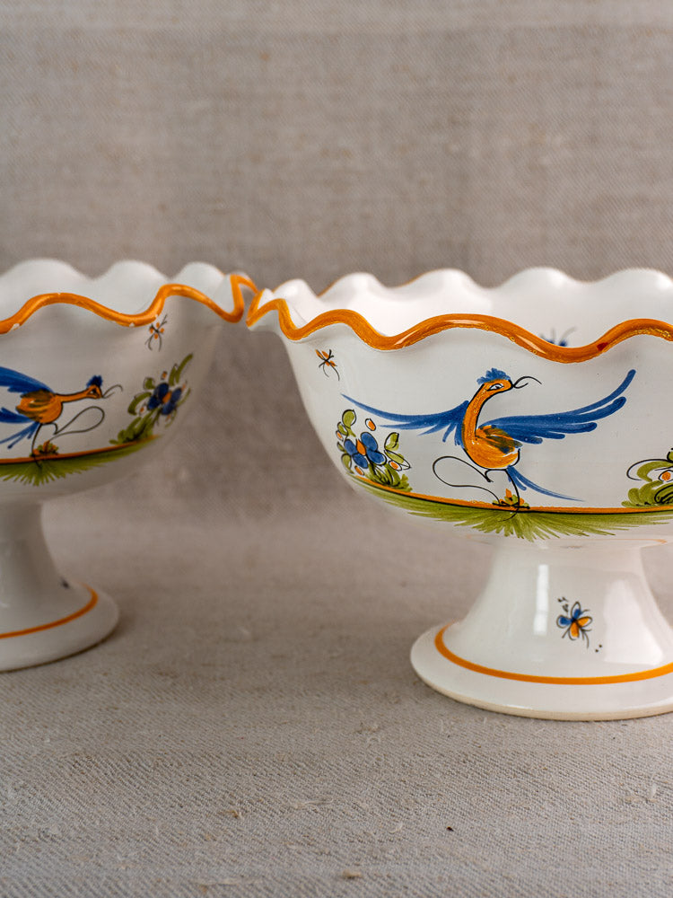 Pair of vintage French Moustiers-style faience compotes with hand-painted birds, flowers, and insects on fabric background.