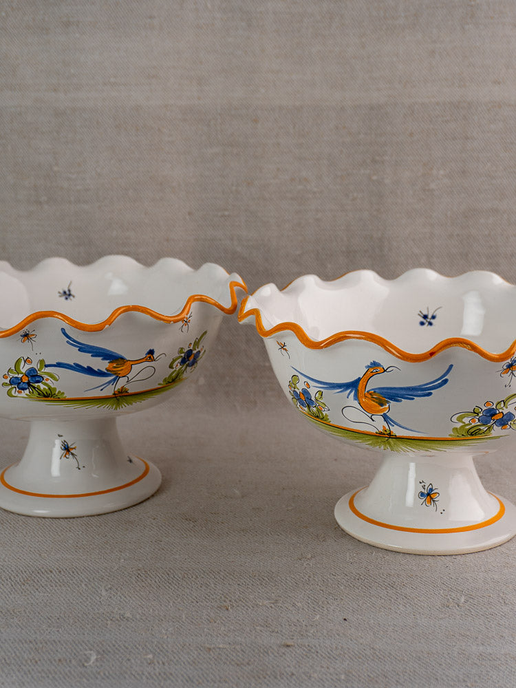 Pair of vintage French Moustiers-style faience compotes with scalloped rims and painted bird motifs.