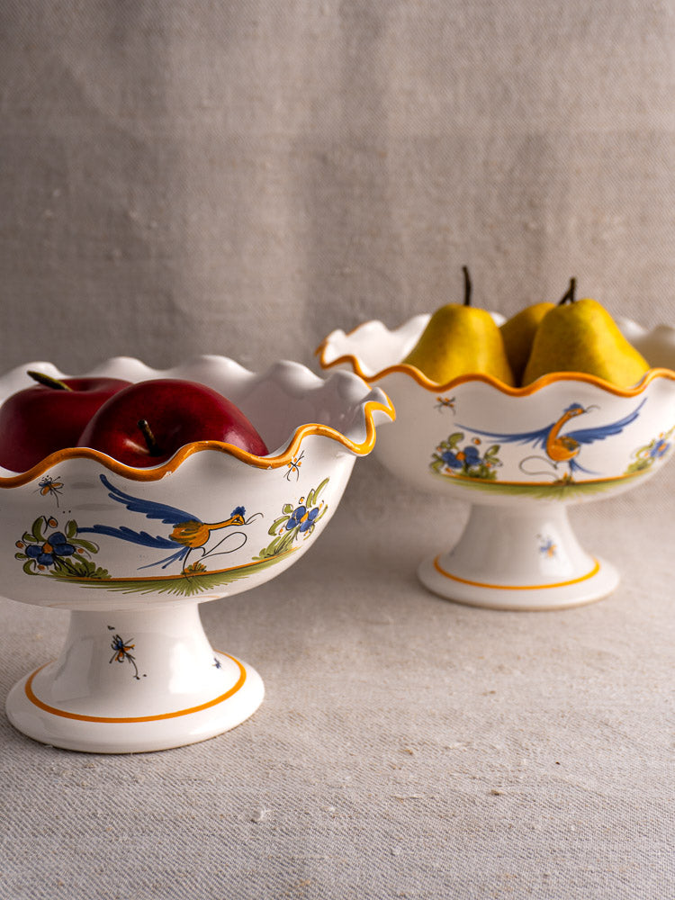 Pair of French Moustiers-style faience compotes with bird and floral motifs, apples and pears displayed.