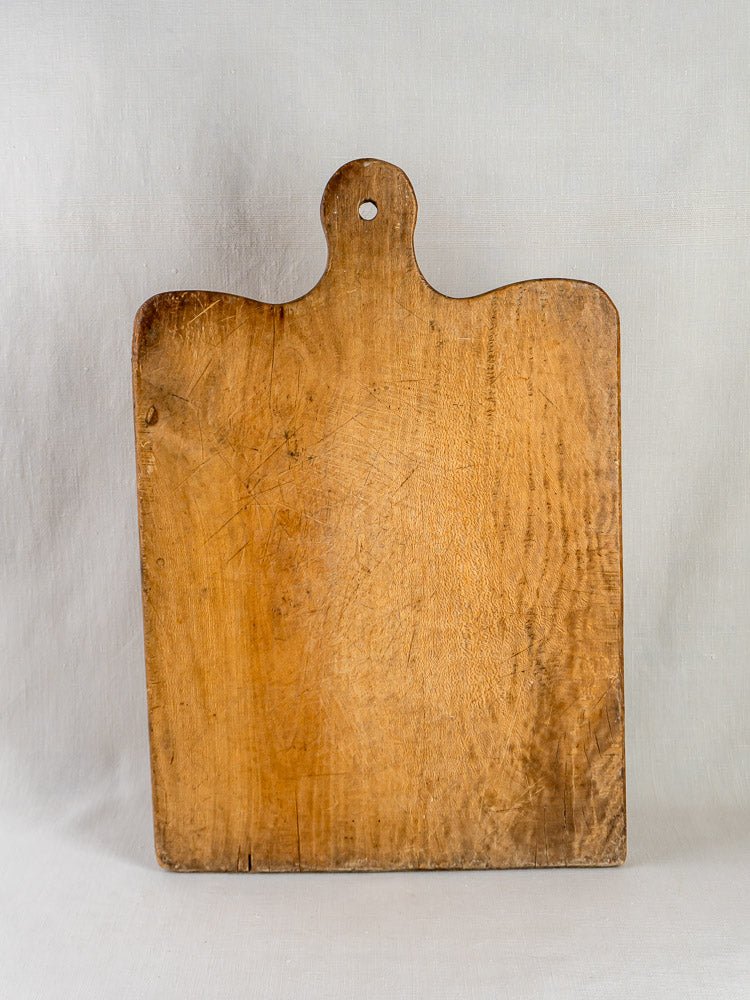 Large 19th-century French hardwood chopping board with handle, upright on light surface, neutral background.