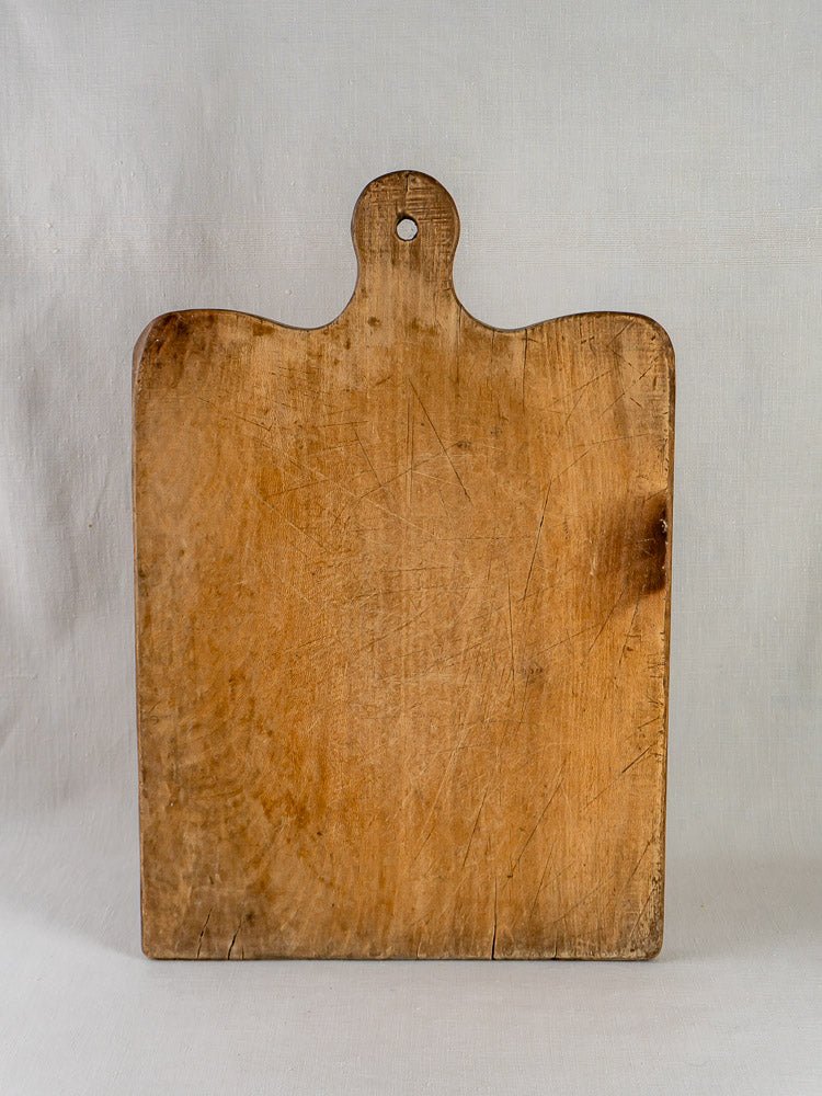 Large 19th-century French hardwood chopping board with rounded handle, hanging hole, and well-worn surface.