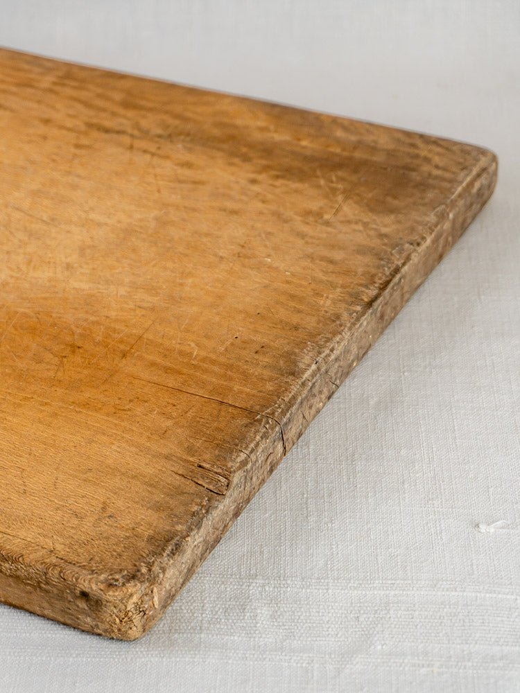 Large antique French hardwood chopping board with timeworn surface on a light textured fabric.